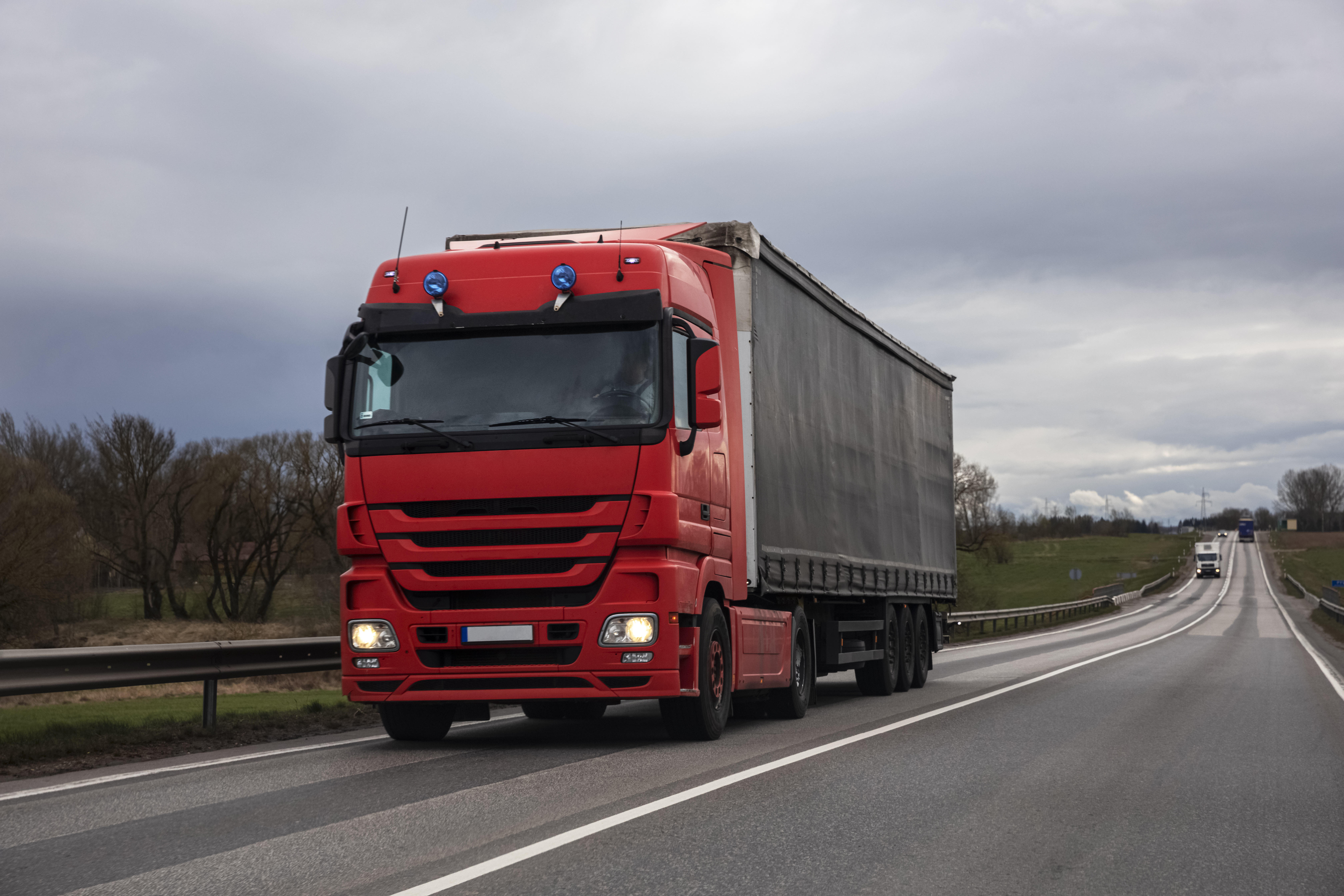 Red articulated lorry driving on a UK motorway under cloudy skies, representing the haulage industry affected by driver shortages.